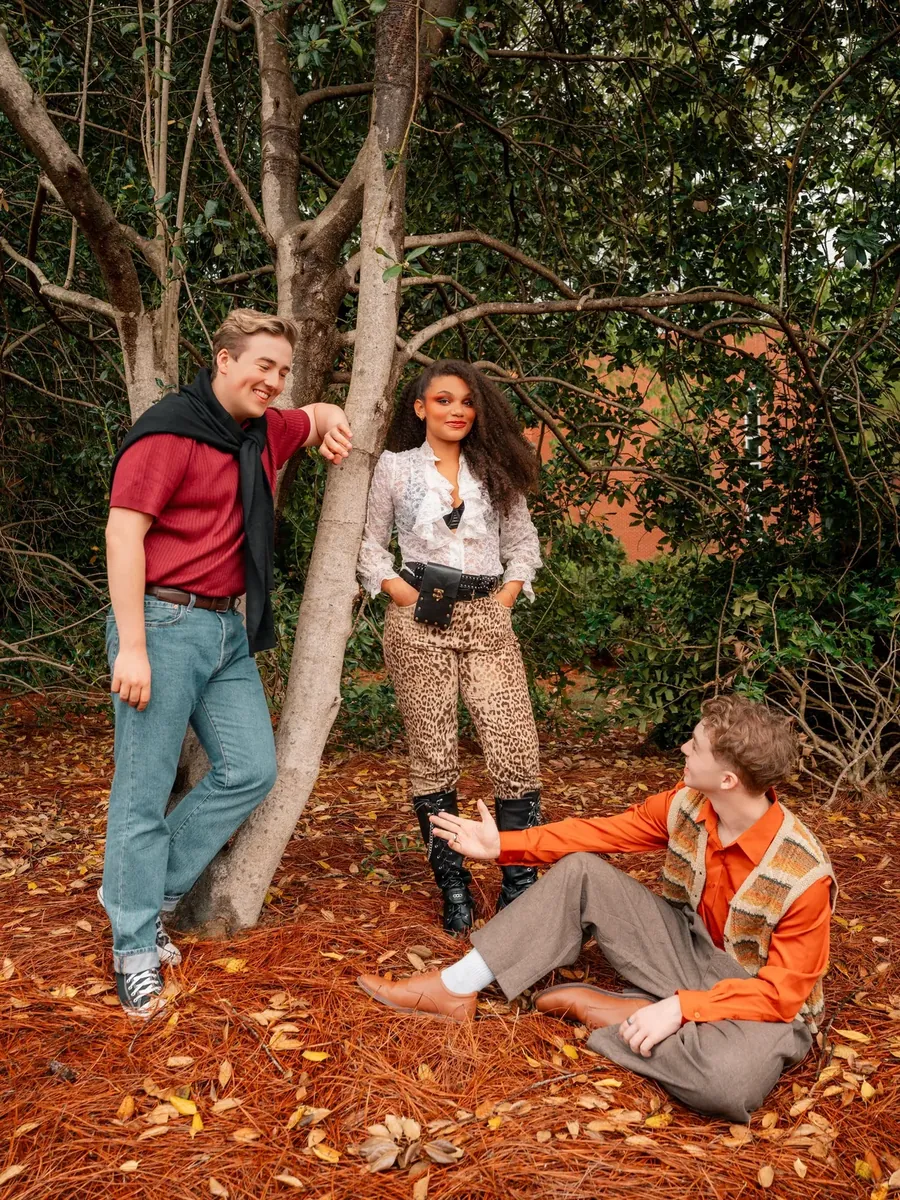 Three of the company share a charged moment among the trees in full costume.