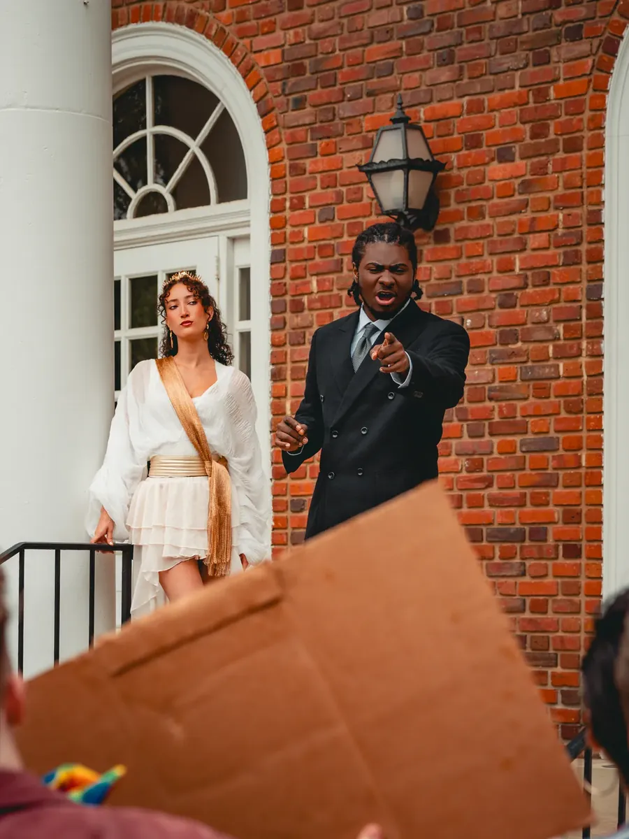 The Oracle in white watches as a suited man points and shouts on the Capitol steps.