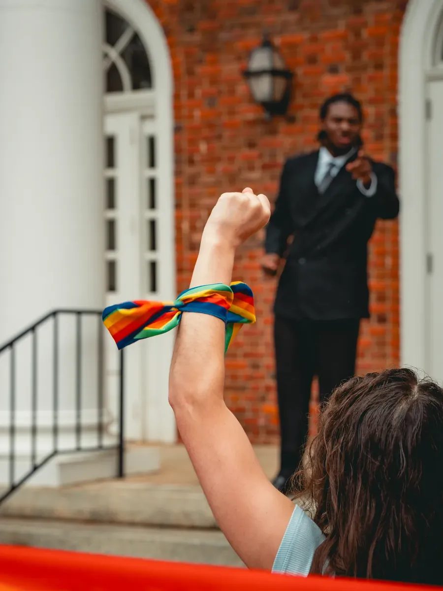 A raised fist wrapped in a rainbow band as an official points back from the steps.