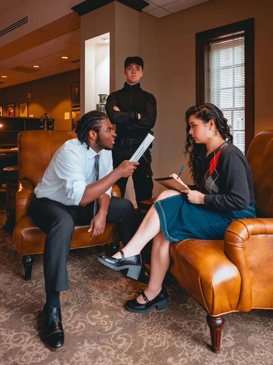 A tense interrogation in a wood-panelled office, a guard standing watch.
